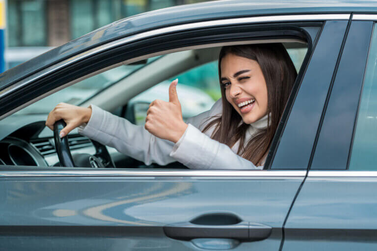 Frau hebt glücklich den Daumen in einem Auto.